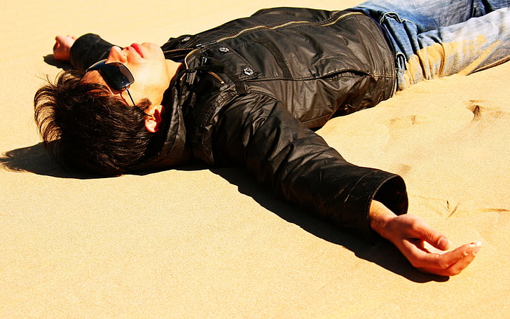 men's black frame sunglasses and black leather jacket, man, lying, sand, beach, jacket, HD wallpaper