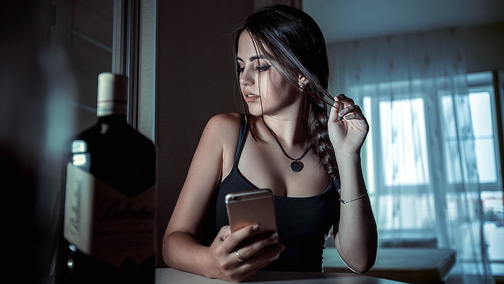 women's black spaghetti strap top, woman in black spaghetti strap top, women, portrait, necklace, cellphone, bottles, looking away, Ballantines, whisky, braids, iPhone, model, touching hair, holding hair, Black top, sitting, open mouth, HD wallpaper