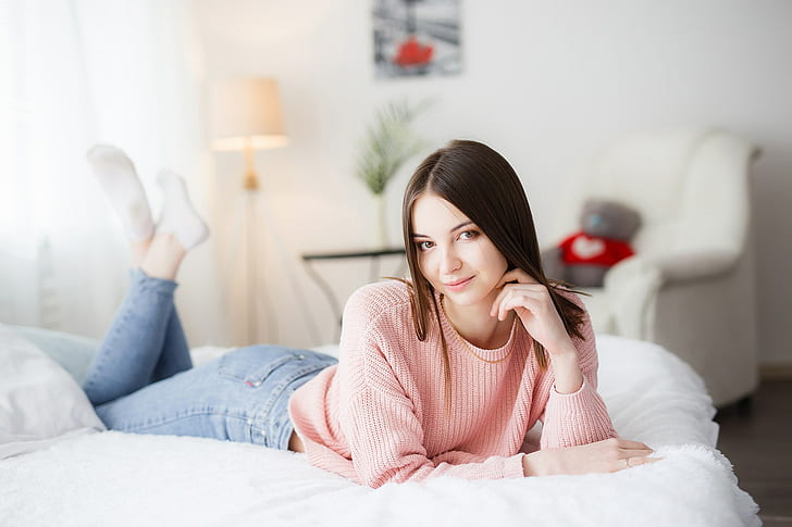 women, model, portrait, indoors, bed, looking at viewer, lying on front, in bed, jeans, socks, sweater, depth of field, feet in the air, brunette, smiling, women indoors, bedroom, pink sweater, touching face, legs up, HD wallpaper