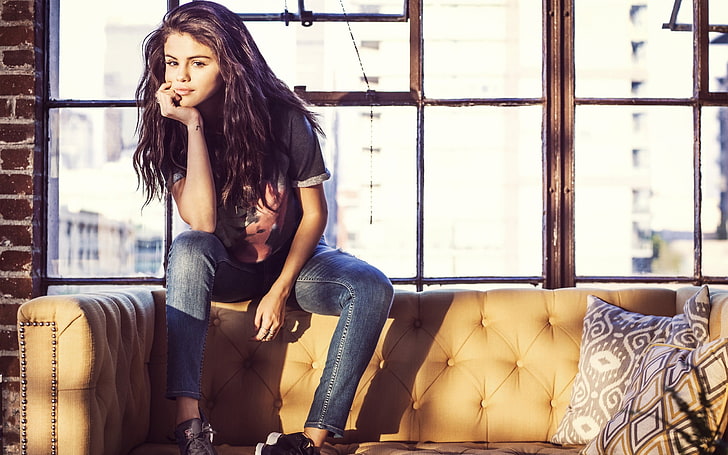 Selena Gomez souriante, femmes, brune, Selena Gomez, cheveux longs, T-shirt, jeans, jambes écartées, main sur le visage, Fond d'écran HD