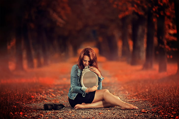 women's black skirt, woman in blue denim jacket and black mini skirt holding oval mirror sitting in the middle of pathway in forest, women, model, long hair, women outdoors, sitting, barefoot, closed eyes, mirror, skirt, leaves, trees, fall, redhead, red leaves, depth of field, HD wallpaper