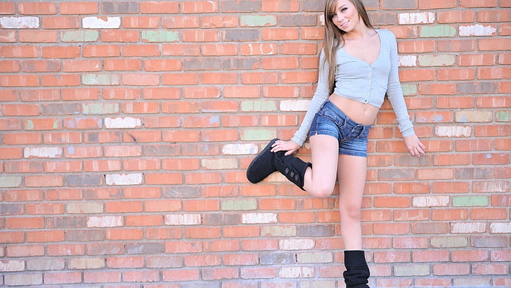 women's gray button-up long-sleeved crop top, woman in grey button-up long-sleeved cardigan and blue-washed denim shorts with pair of black boots standing beside cladding wall, pornstar, jean shorts, Capri Anderson, brunette, women, UGG Boots, wall, model, smiling, boots, HD wallpaper