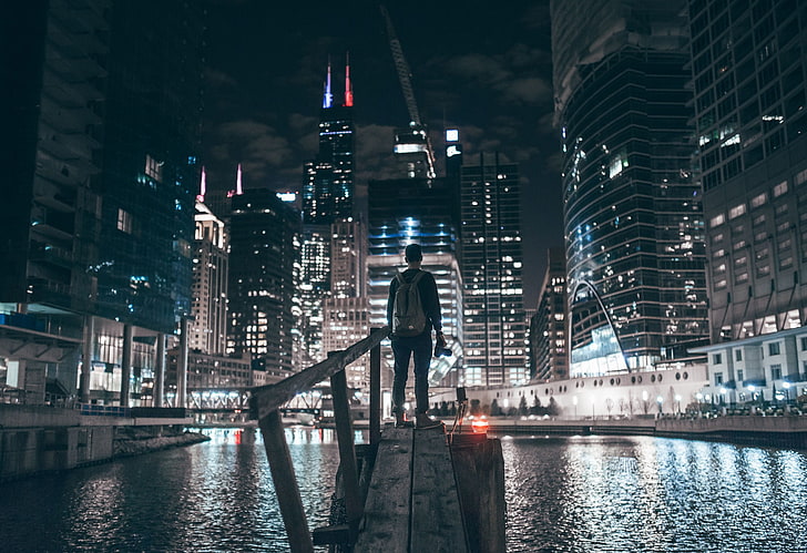 gray backpack, standing man in wooden dock carrying brown backpack photo taken during nighttime, cityscape, night, skyscraper, city lights, Chicago, river, cranes (machine), HD wallpaper