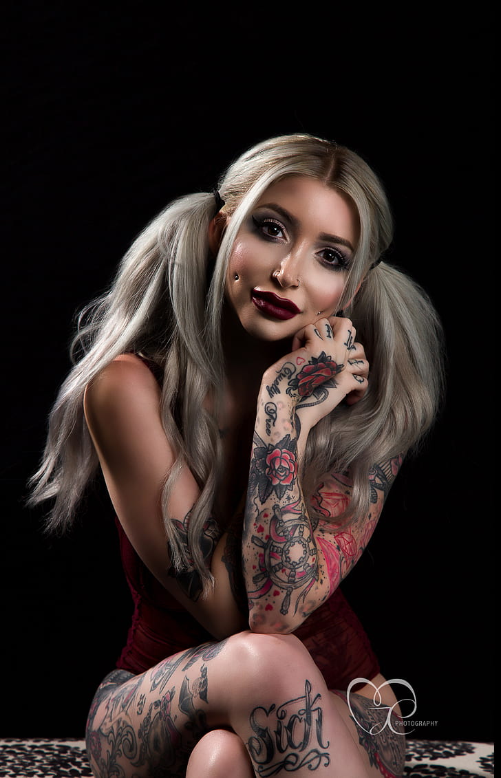women, model, long hair, pigtails, blonde, straight hair, dyed hair, tattoo, ink, young woman, looking at viewer, sitting, dark background, black background, simple background, arms crossed, lipstick, red lipstick, dark lipstick, mascara, eyeshadow, eyelashes, makeup, pierced nose, nose ring, watermarked, corset, dark eyes, women indoors, legs crossed, vertical, touching face, pierced cheeks, HD wallpaper