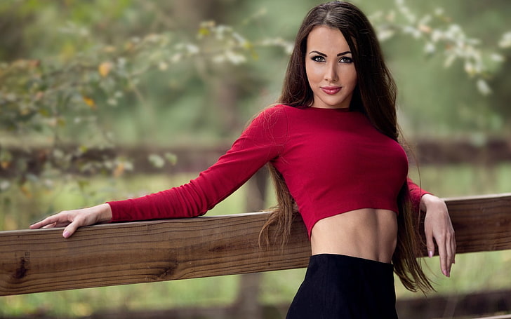 women's red long-sleeved crop top, selective focus photograph of woman leaning on lumber, women, model, brunette, long hair, women outdoors, looking at viewer, nature, trees, Leah Serres, skirt, wood, depth of field, straight hair, makeup, red tops, bare midriff, HD wallpaper
