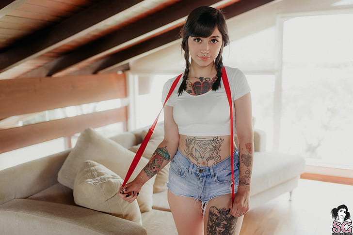 Dawud Suicide, women, model, brunette, braids, portrait, looking at viewer, brown eyes, standing, indoors, pierced septum, smiling, white tops, jean shorts, suspenders, belly, depth of field, couch, cushions, inked girls, tattoo, black nails, women indoors, Suicide Girls, eyeliner, HD wallpaper