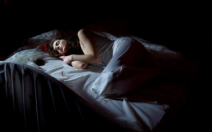 жена, лежаща върху бяло спално бельо, жени, модел, брюнетка, дълга коса, бяла рокля, спане, затворени очи, в леглото, черен фон, HD тапет