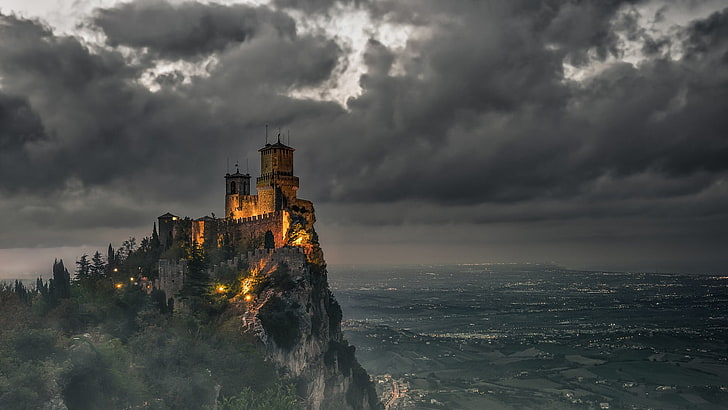 brown concrete castle, brown castle on edge of cliff with sea at the bottom, nature, landscape, architecture, castle, clouds, lights, tower, San Marino, rock, trees, hills, field, cityscape, dark, HD wallpaper