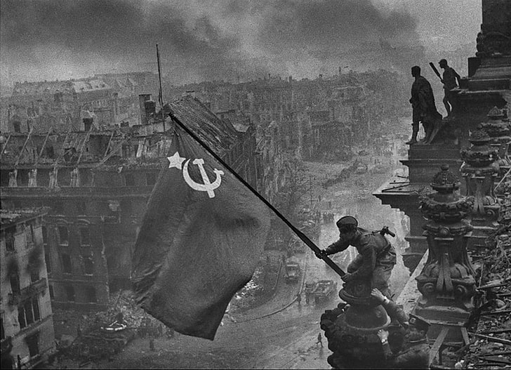 Person, die die Flagge am 9. Mai, dem Tag des Sieges, der Flagge über dem Reichstag, auf der Gebäudemalerei steht, HD-Hintergrundbild
