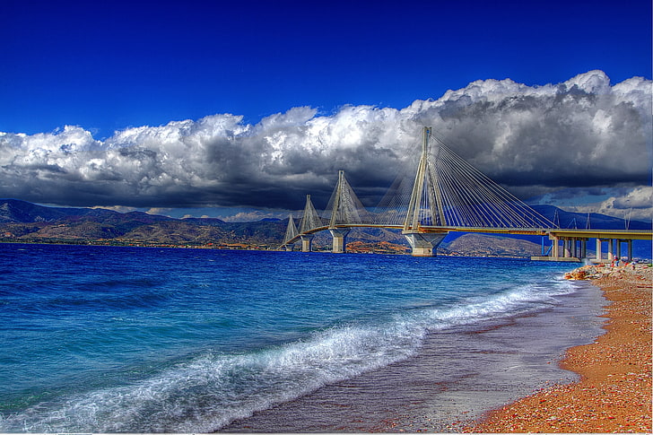 Foto de vista de puente gris y negro y orilla del mar, el cielo, el agua, las nubes, el puente, los guijarros, la costa, de color, Grecia, Río-Antirio, el Golfo de Corinto, cable, 