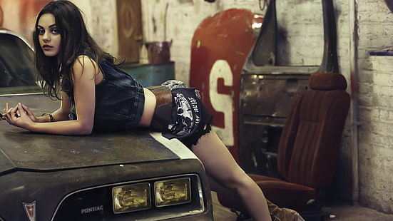 Mila Kunis, wanita yang bersandar pada mobil Pontiac hitam, Mila Kunis, wanita, aktris, wanita dengan mobil, berambut cokelat, garasi, beige, membungkuk, rok mini, Wallpaper HD HD wallpaper