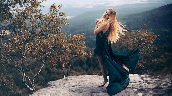 women's blue sleeveless slit dress, woman wearing teal sleeveless dress posing with both of her hands on her heart while she close her eyes on grey cliff surrounded with brown trees, women, model, blonde, long hair, women outdoors, nature, rock, trees, landscape, forest, dress, closed eyes, barefoot, fall, leaves, bare shoulders, windy, HD wallpaper HD wallpaper