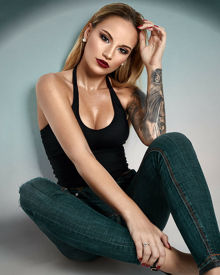 Javier Ullastres, women, blonde, long hair, straight hair, jewelry, earring, beads, painted nails, red nails, long nails, make up, eyeshadow, eyeliner, lipstick, lip gloss, piercing, pierced nose, looking at viewer, tank top, black clothing, cleavage, jeans, denim, rings, tattoo, wall, sweat, body oil, HD wallpaper